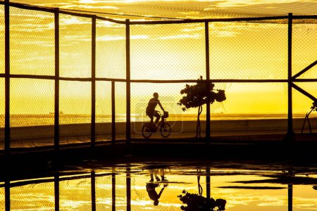 Téléchargez les photos : Cycliste faisant de l'exercice sur le bord de la plage du Rio Vermelho contre le coucher du soleil. Ville de Salvador, Bahia. - en image libre de droit