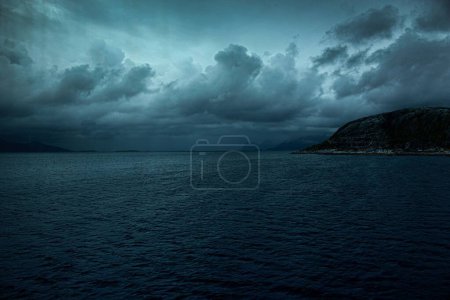 Téléchargez les photos : La mer calme avec des montagnes en arrière-plan sous le ciel sombre orageux - en image libre de droit