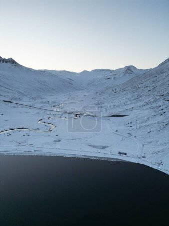 Téléchargez les photos : Vue aérienne du rivage enneigé et du lac sombre. Hedinsfjordur, un fjord désert en Islande. - en image libre de droit
