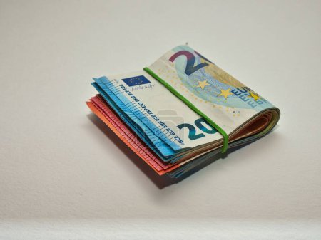 Téléchargez les photos : Une liasse de billets en euros maintenus solidement par un élastique sur fond blanc - en image libre de droit