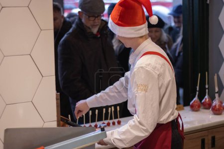 Téléchargez les photos : Un jeune homme avec un chapeau rouge qui fait des sucettes à un marché de Noël à Madrid, Espagne - en image libre de droit