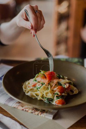 Photo for A close-up shot of tagliatelle pasta with cherry sauce, female hand eating with a fork - Royalty Free Image
