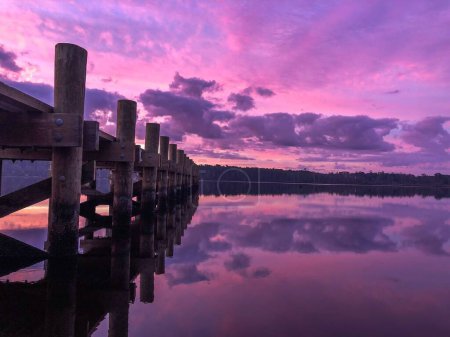 Téléchargez les photos : Un coucher de soleil violet envoûtant sur la rive du lac avec une jetée - en image libre de droit