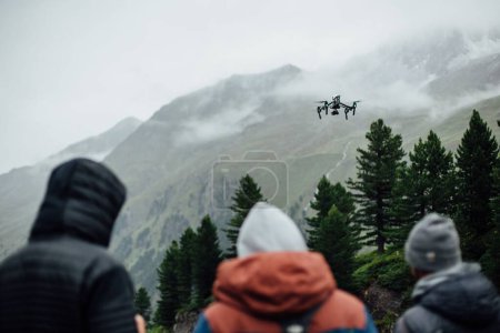 Photo for The people watching the drone flying over the trees and mountains covered in fog. - Royalty Free Image