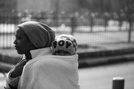 Téléchargez les photos : Une échelle de gris d'une mère portant un bébé garçon avec la manière traditionnelle dans une couverture à l'arrière dans la ville de Jérusalem, Israël - en image libre de droit