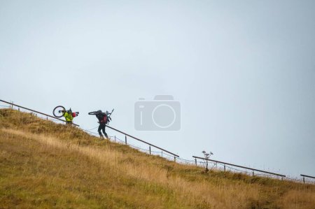 Téléchargez les photos : Deux cyclistes montant une colline en vélo par une journée nuageuse à la campagne - en image libre de droit