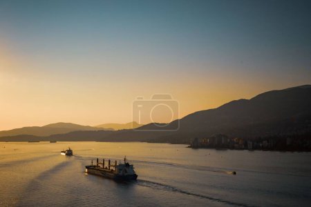 Foto de Una vista aérea de un barco navegando en un mar cerca de un puerto contra las montañas al atardecer - Imagen libre de derechos