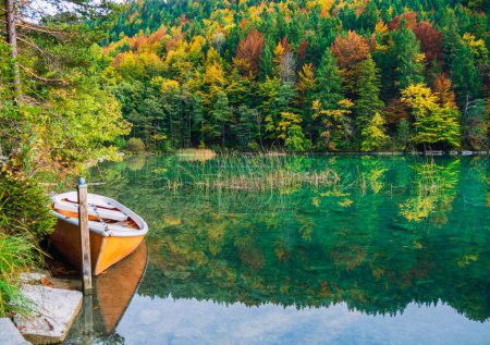 Téléchargez les photos : Un petit bateau sur un lac clair et calme avec le reflet des arbres dans l'eau - en image libre de droit