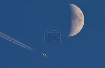 Téléchargez les photos : Un avion volant devant la lune avec une traînée de jet derrière lui - en image libre de droit