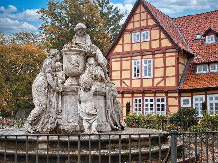 Téléchargez les photos : Une statue de femmes et d'enfants par une clôture avec une maison à ossature rouge derrière - en image libre de droit
