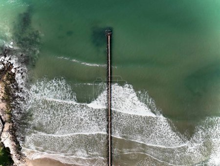 Téléchargez les photos : Une vue aérienne d'une longue jetée entourée d'eau tranquille sur une plage de sable - en image libre de droit