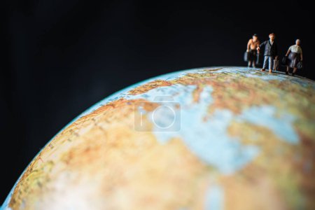 Téléchargez les photos : Un gros plan de personnes miniatures tenant des bagages marchant sur une surface du globe - en image libre de droit