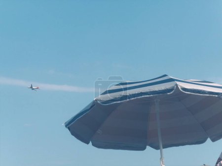 Photo for A plane flying over a beach with a blue and white umbrella - Royalty Free Image