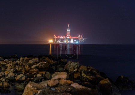 Téléchargez les photos : Une plate-forme pétrolière offshore la nuit avec des lumières réfléchies dans l'eau - en image libre de droit