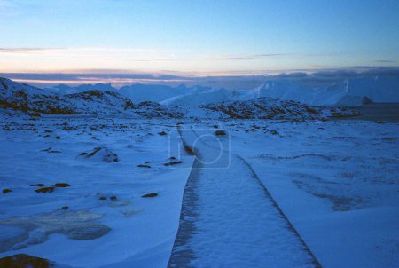 Téléchargez les photos : Une belle vue sur un sentier dans un champ enneigé avec des collines au lever du soleil - en image libre de droit