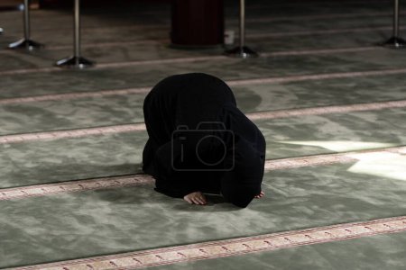 Foto de Una mujer musulmana vestida de negro con hiyab rezando en una mezquita. - Imagen libre de derechos