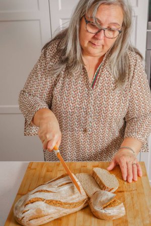 Foto de Mujer de pelo blanco cortando rebanadas de pan casero recién horneado - Imagen libre de derechos