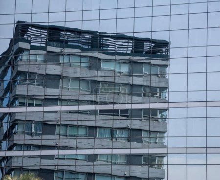 Téléchargez les photos : Un bâtiment déformé qui se reflète dans la façade d'un grand bâtiment avec des fenêtres - en image libre de droit