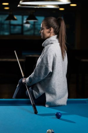 Photo for A vertical shot of a young woman sitting on the pool table. - Royalty Free Image