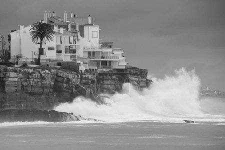 Téléchargez les photos : Un plan en niveaux de gris des bâtiments au bord de la mer pendant les vagues orageuses - en image libre de droit