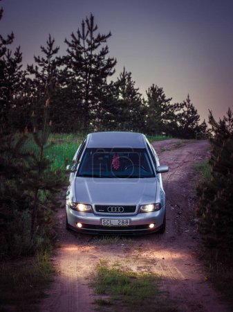 Téléchargez les photos : Une Audi A4 B5 verticale argentée sur un chemin de terre descendant avec phares allumés - en image libre de droit