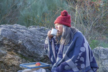 Téléchargez les photos : Femme aux cheveux blancs et casquette rouge buvant du café dans un champ avec un plateau de fruits - en image libre de droit