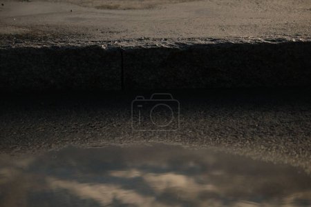 Téléchargez les photos : Un gros plan d'eau dans un nid de poule sur une route asphaltée - en image libre de droit