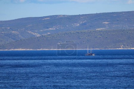 Téléchargez les photos : Un bateau naviguant dans un océan avec des montagnes couvertes d'arbres en arrière-plan - en image libre de droit