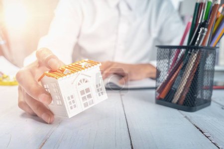 Téléchargez les photos : Un agent immobilier tenant un modèle de petite maison sur son bureau - concept immobilier - en image libre de droit