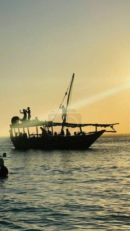 Téléchargez les photos : La silhouette d'un navire avec des gens joyeux au coucher du soleil à Kendwa Beach, île de Zanzibar - en image libre de droit