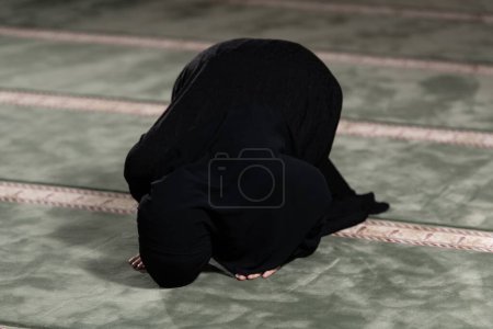 Téléchargez les photos : Une femme musulmane en robe noire avec hijab priant dans une mosquée. - en image libre de droit