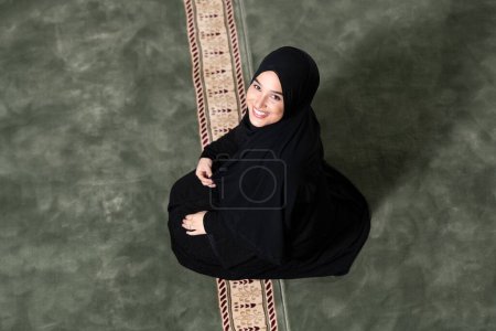 Téléchargez les photos : Plan en grand angle d'une belle musulmane vêtue d'une robe noire avec hijab priant dans une mosquée. - en image libre de droit