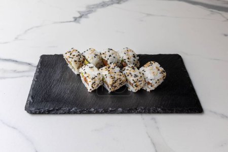 Photo for A set of California rolls in sesame seeds served on the black board on the marble table - Royalty Free Image