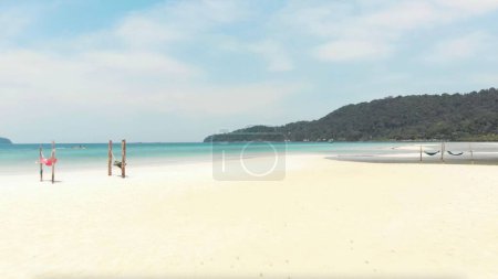 Photo for An beautiful view of Koh Rong beach in Cambodia surrounded by green grasses and swings under a blue sky - Royalty Free Image