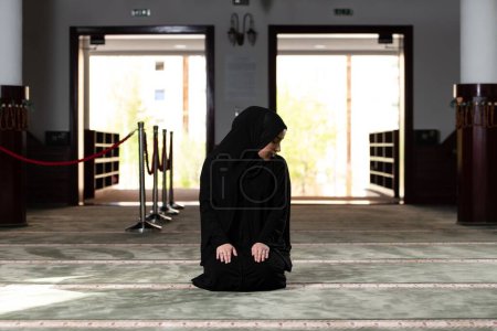 Foto de Una hermosa mujer musulmana en una mezquita con un vestido negro con hiyab. Fe musulmana, cultura. - Imagen libre de derechos