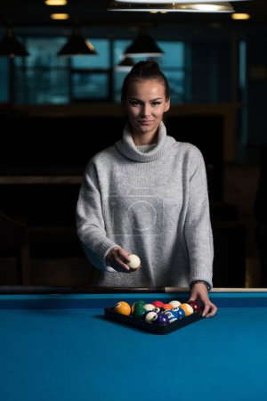 Photo for A young woman standing at the pool table arranging billiard balls in a triangle. - Royalty Free Image