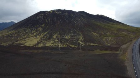 Téléchargez les photos : Une route asphaltée passant par une montagne volcanique couverte de mousse verte et un champ de lave noire à Landmannalaugar, Islande - en image libre de droit