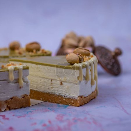 Foto de Un primer plano de la pieza de un pastel de queso con crema de pistacho decorado con pistachos y crema de vainilla sobre un fondo borroso - Imagen libre de derechos