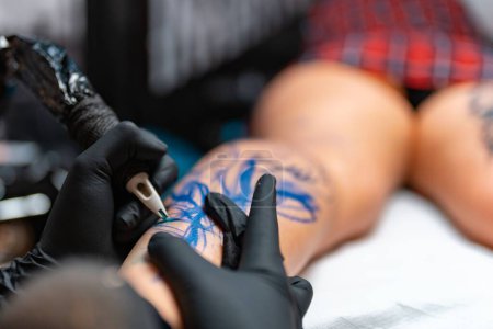 Photo for A closeup of a tattoo artist doing a tattoo art on a woman's leg at the salon - Royalty Free Image