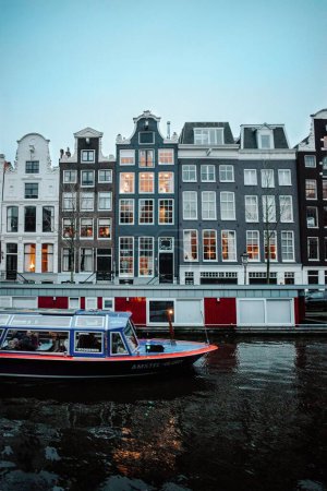 Photo for A vertical shot of the boat in river with Famous looking buildings in Amsterdam - Royalty Free Image