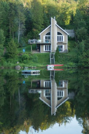 Eine vertikale Aufnahme eines Einfamilienhauses am Flussufer mit der Spiegelung seines Bildes im See in Mont Tremblant, Kanada