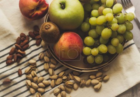Photo for A closeup top view of fruit and nuts on a towel and a metal fork next to the plate - Royalty Free Image