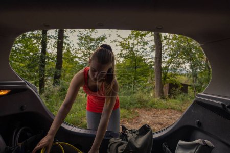 Téléchargez les photos : La fille dans la forêt obtenant l'équipement d'escalade du coffre d'une voiture. - en image libre de droit