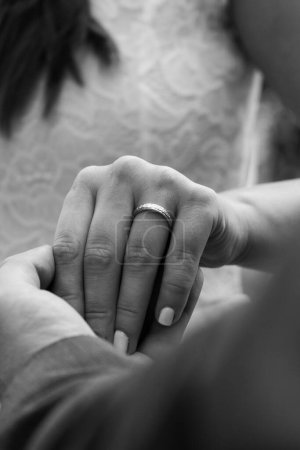 Téléchargez les photos : Un gros plan en niveaux de gris d'une main masculine tenant une main féminine avec une bague de mariage dessus, fond flou - en image libre de droit