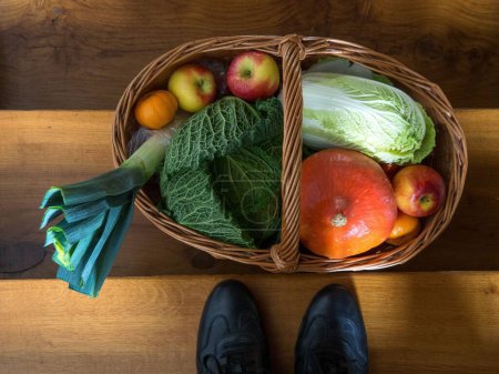 Téléchargez les photos : L'homme se tient devant le panier plein avec différents types de légumes sur les escaliers en bois - en image libre de droit