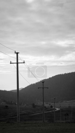 Téléchargez les photos : Une échelle de gris de champs avec des lignes électriques et des stations autour, montagnes et fond de ciel ensoleillé - en image libre de droit