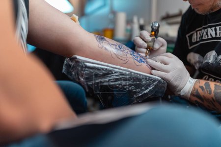 Téléchargez les photos : Un jeune homme se fait tatouer sur le bras lors d'une convention de tatouage - en image libre de droit