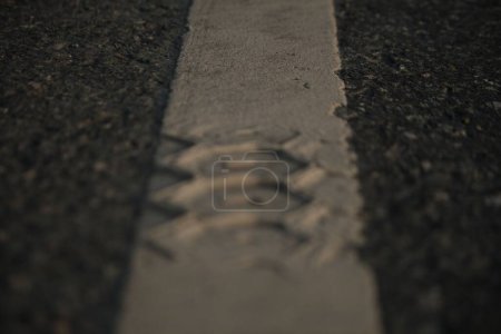 Téléchargez les photos : Mise au point sélective de marques de pneus sur une ligne de marquage blanche sur une route asphaltée - en image libre de droit