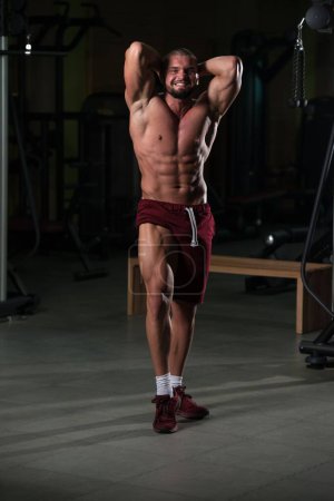 Téléchargez les photos : Un beau jeune homme caucasien debout fort dans le gymnase et les muscles flexibles après les exercices - en image libre de droit
