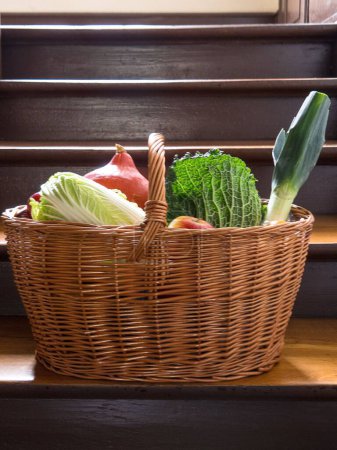 Foto de Una cesta de mimbre con un surtido recién comprado de verduras de pie en un suelo de madera - Imagen libre de derechos